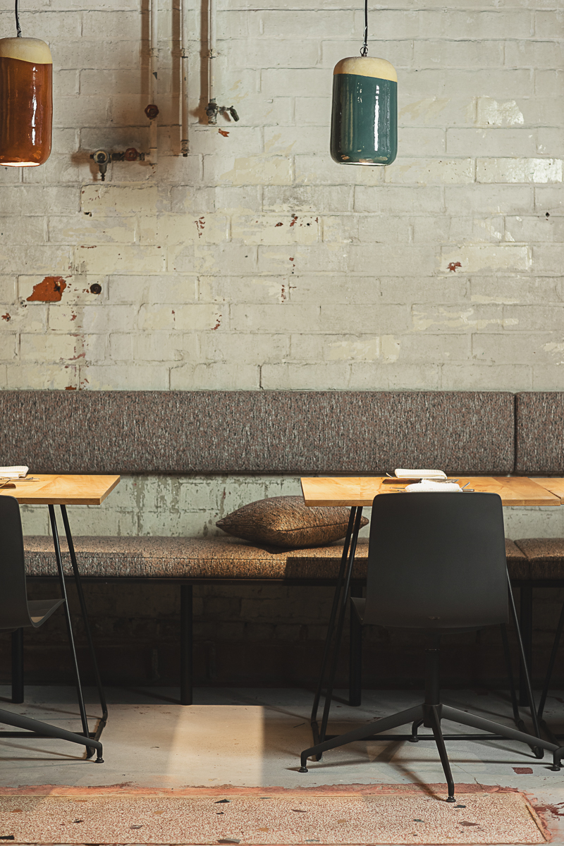 Restaurantinterieur met grijze zitbank, witgekalkte muur en kleurrijke pendelverlichting